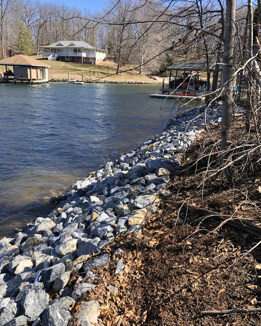 Gray riprap along a steep, wooded cove bank, with lake homes and boathouses across the water