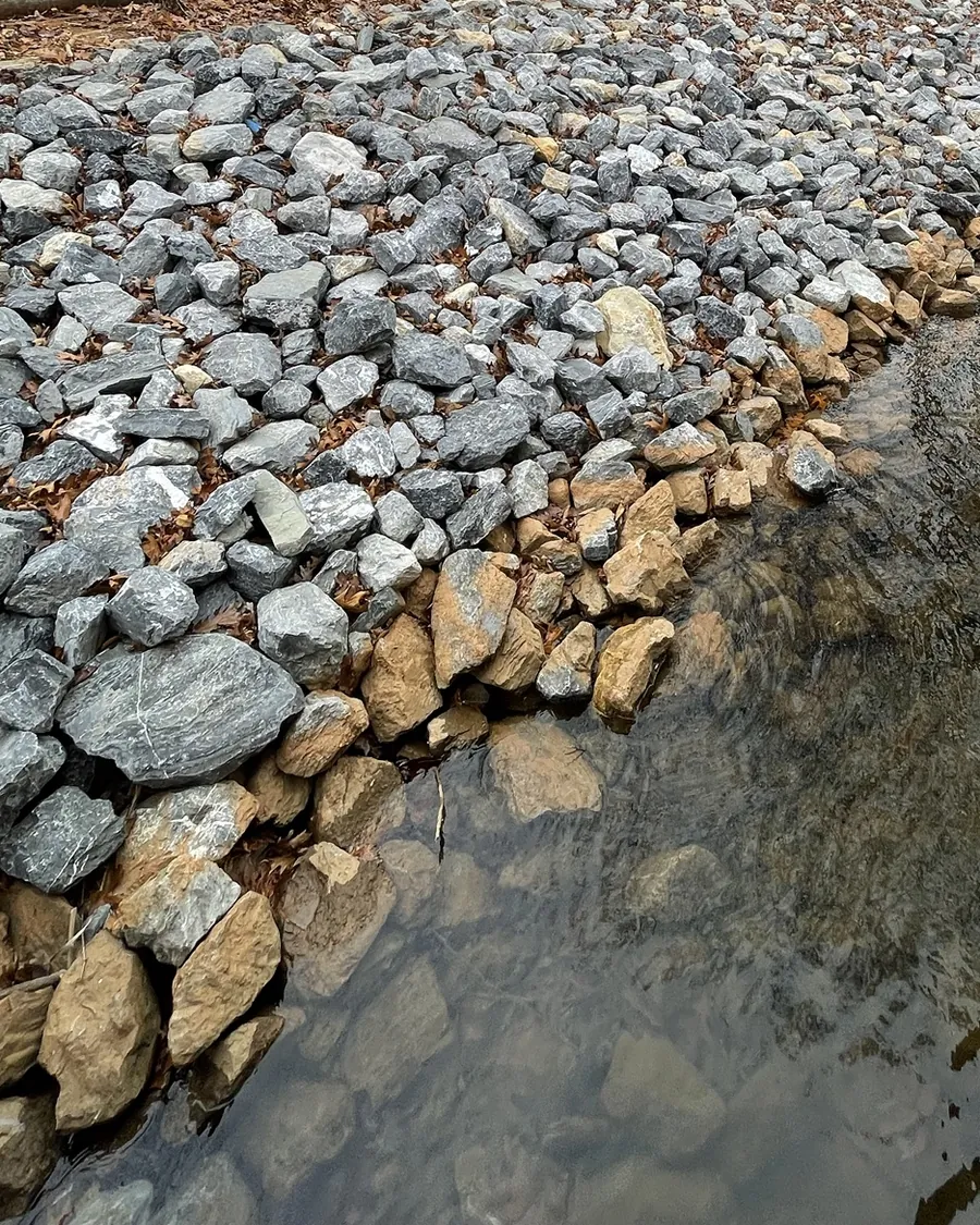 Riprap meeting the water, with a row of larger tan stones along the bottom edge of the slope