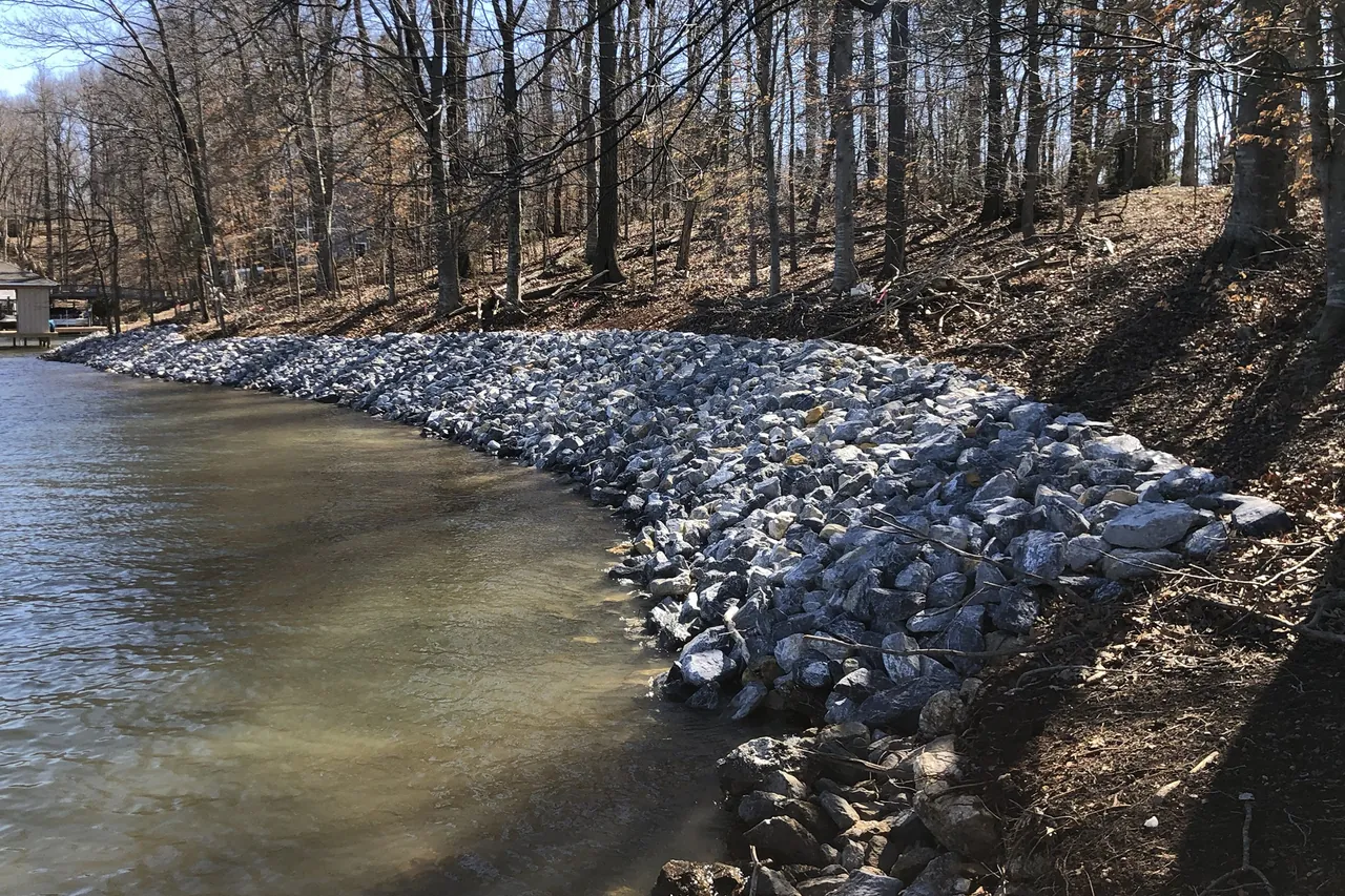 Long run of new gray riprap along a wooded lake bank in winter, with bare trees above the stone